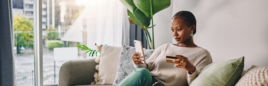 Woman sits on a couch with her credit card and her cell phone.